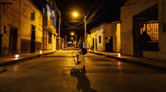 De joelhos no chão, menino ora no meio da rua pelo fim do coronavírus